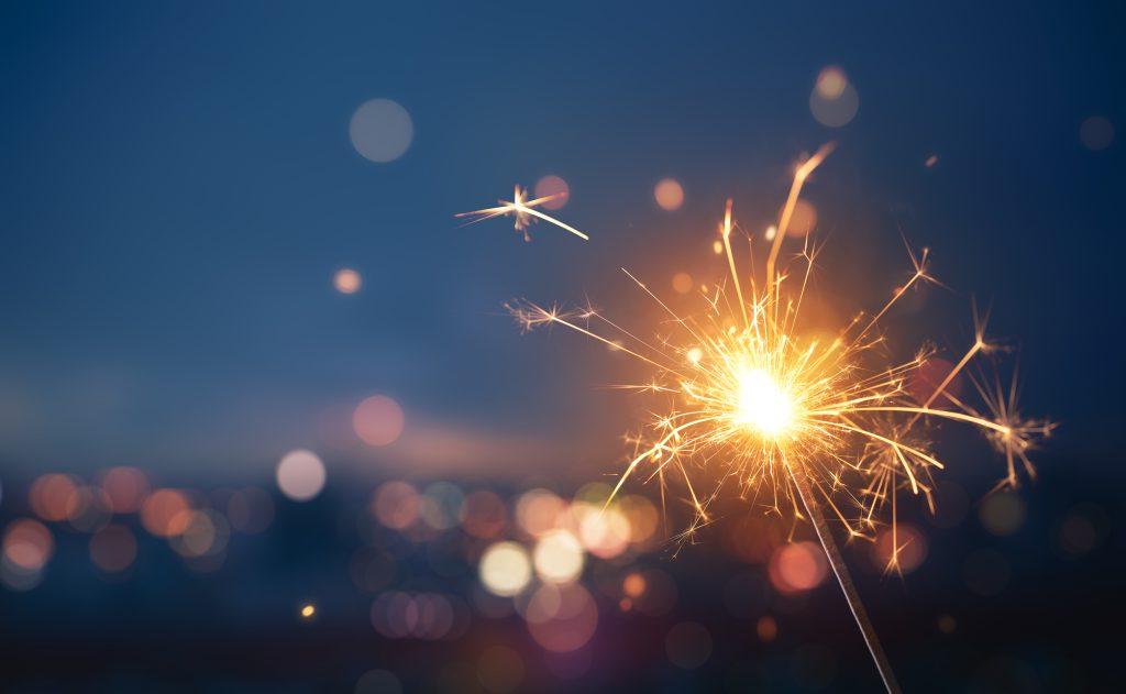 A sparkler firework with the blurred lights of a city in the distance behind it.